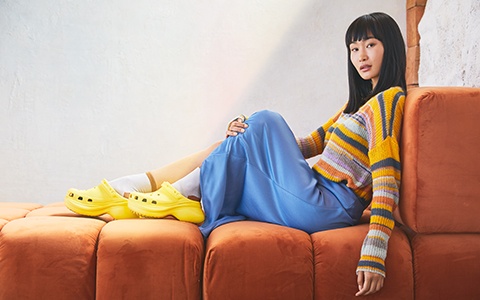 Woman posing on a sofa in the Crocs Classic Bae Clog in Sunshine.