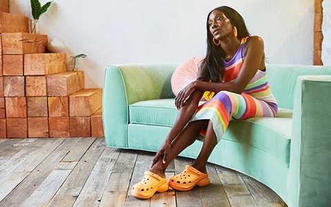 Woman posing on a sofa in the Crocs Classic Bae Clog in Cantaloupe.